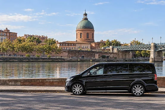 Van Mercedes noir au bord d’un fleuve, face à un dôme en briques.